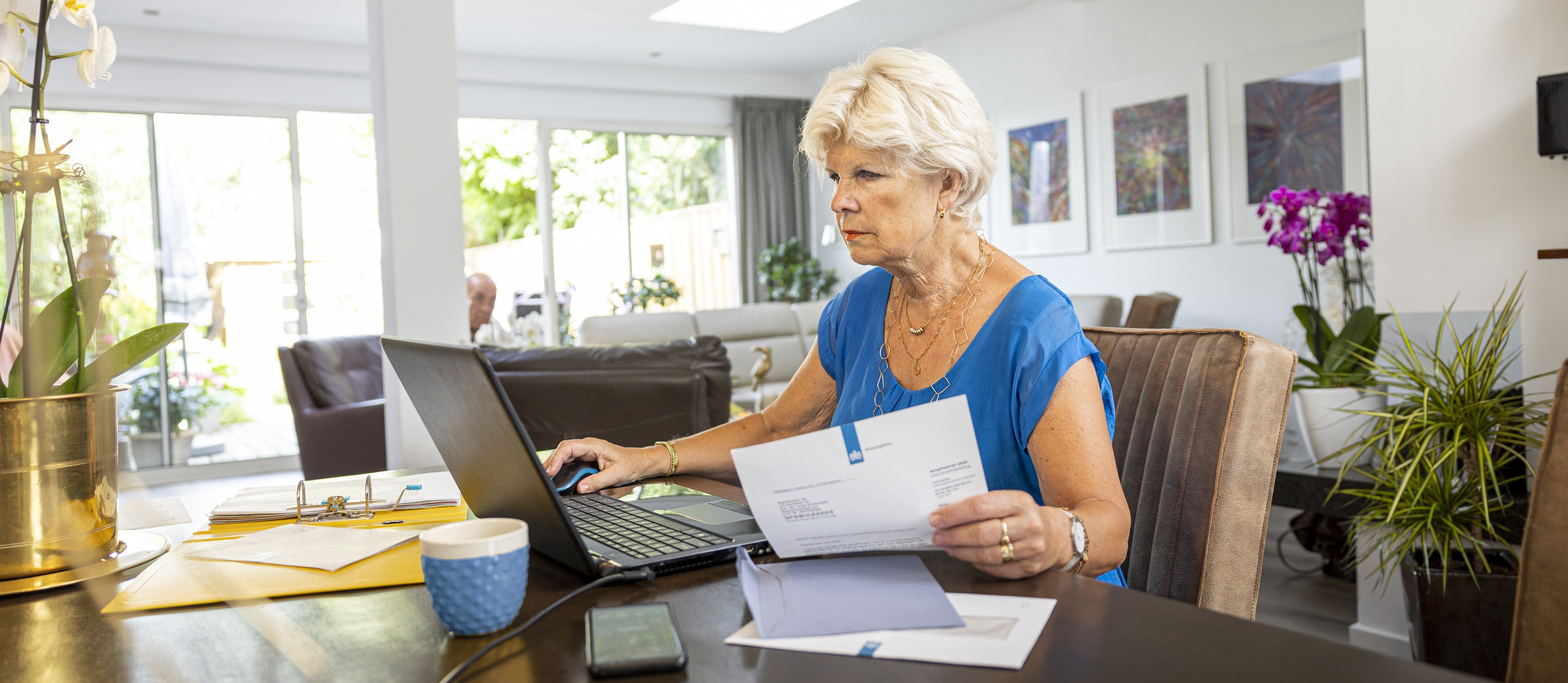 Mevrouw zit op haar laptop in huis met belastingdienst brief in de hand